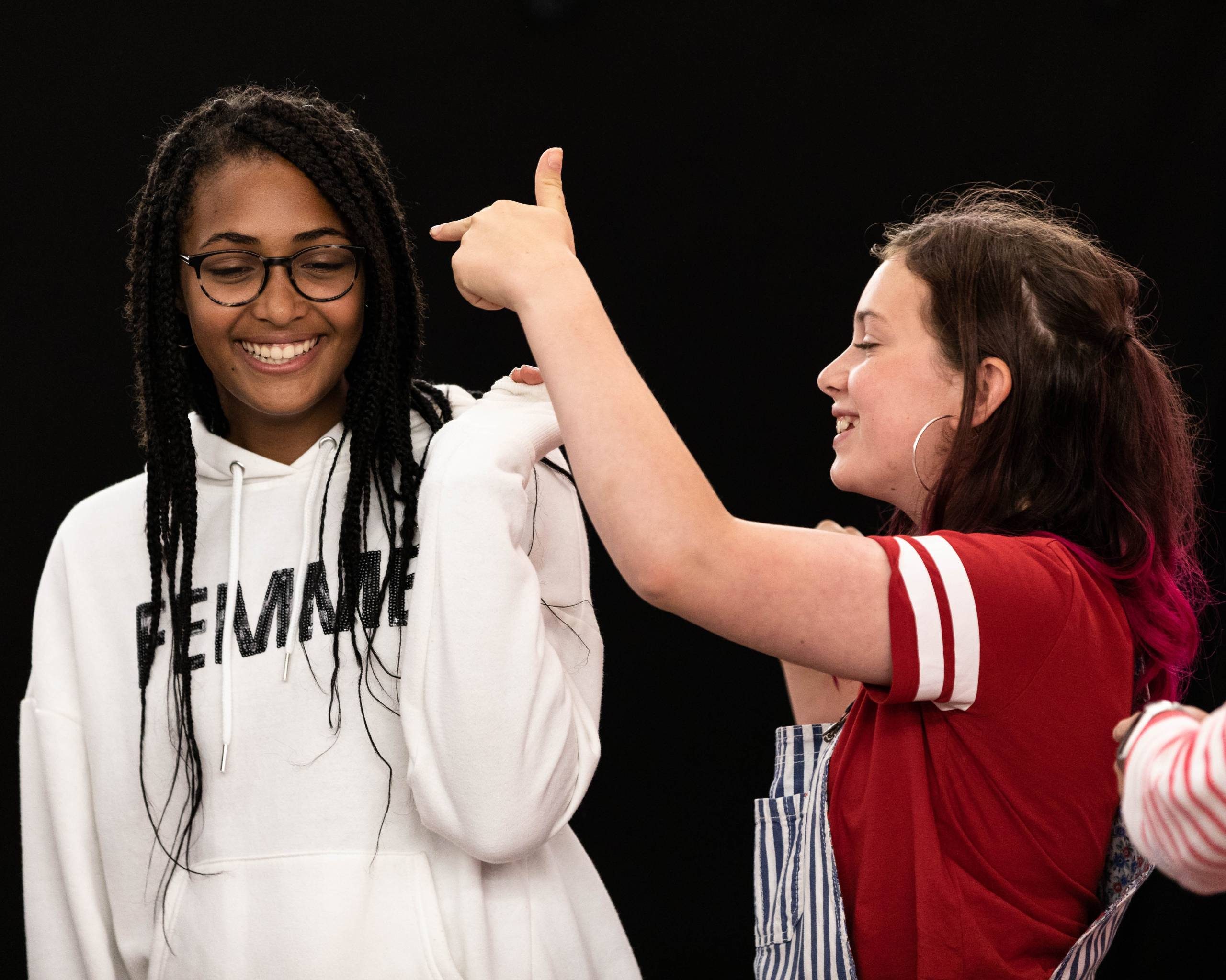 Two young people smile in a workshop against a black wall.
