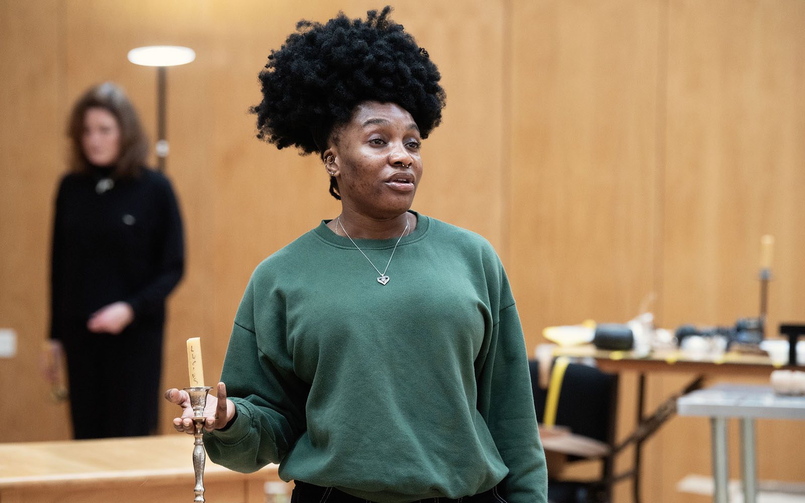 An actor in a green jumper holding a candle in a candlestick.
