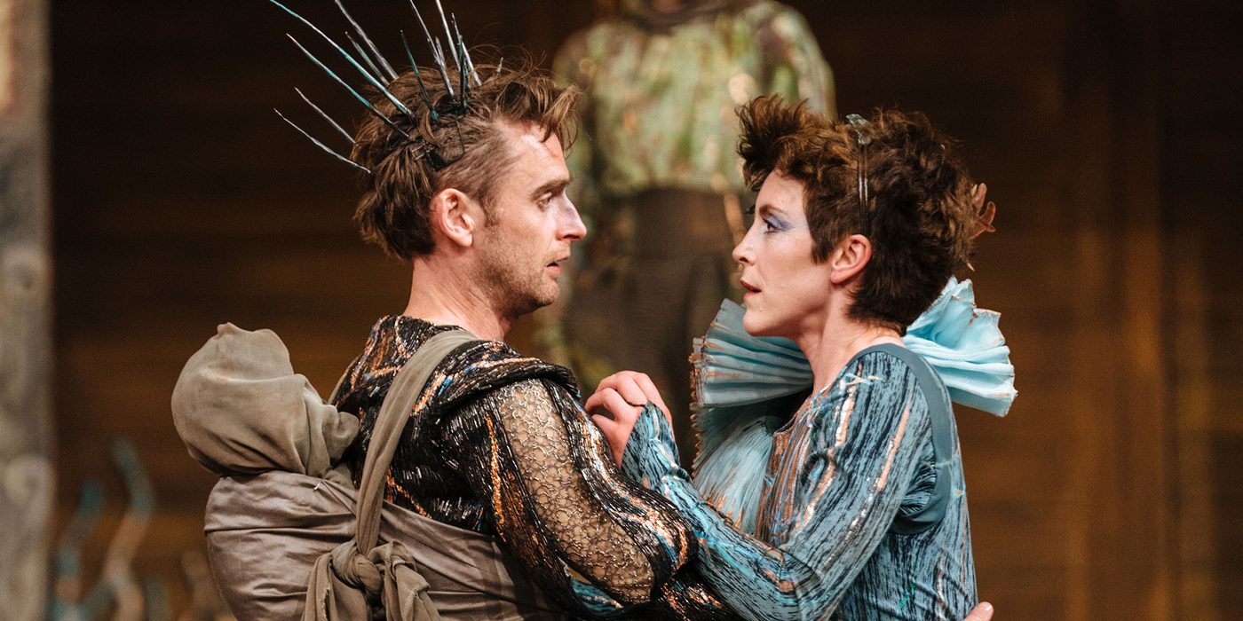 Two actors holding each other, they are both in heavy, fantastical costumes