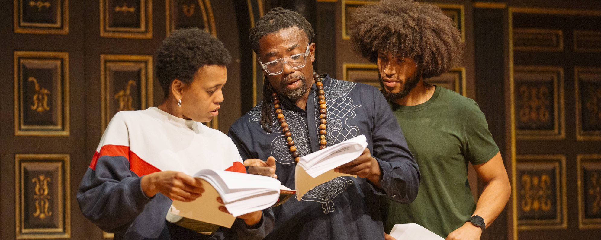 Three people examining scripts on stage in the Sam Wanamaker Playhouse.
