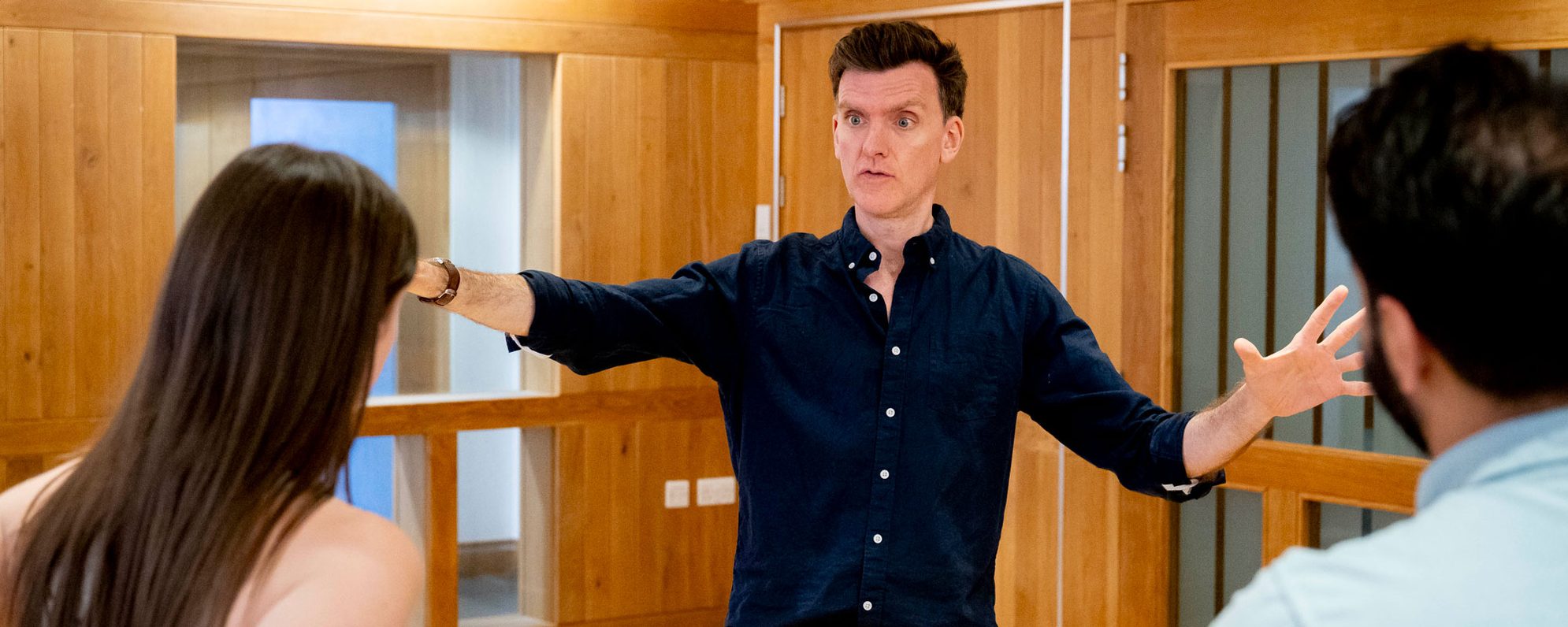 A man in a navy blue shirt delivering training with his arms outstretched enthusiastically