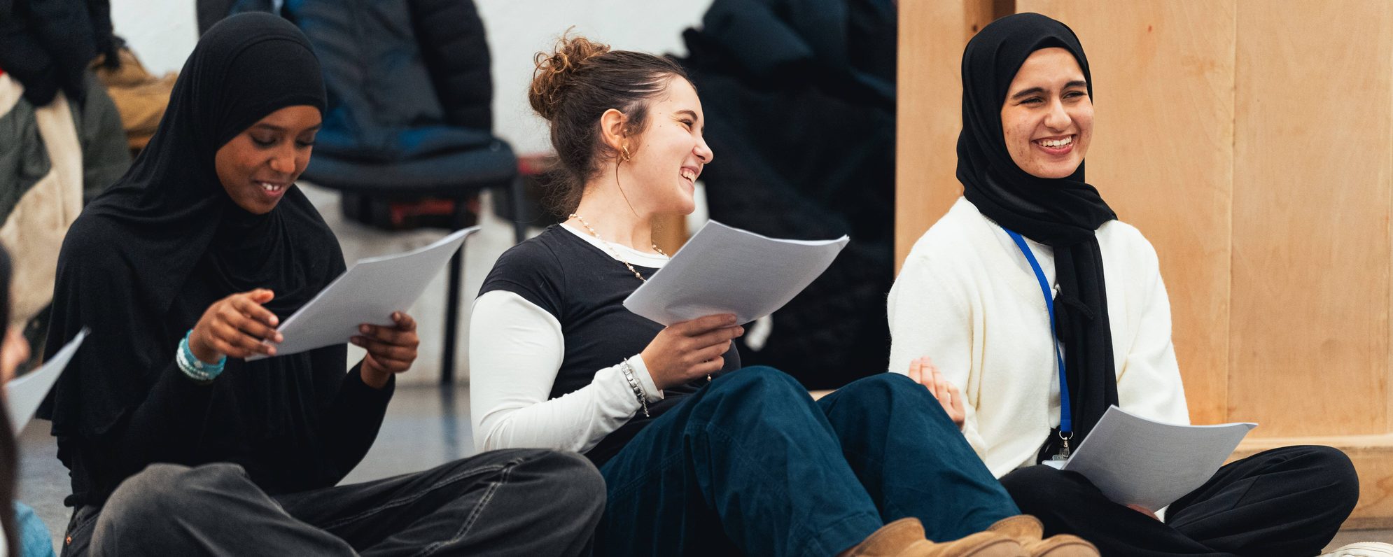 Students in a workshop, laughing as they read together from scripts