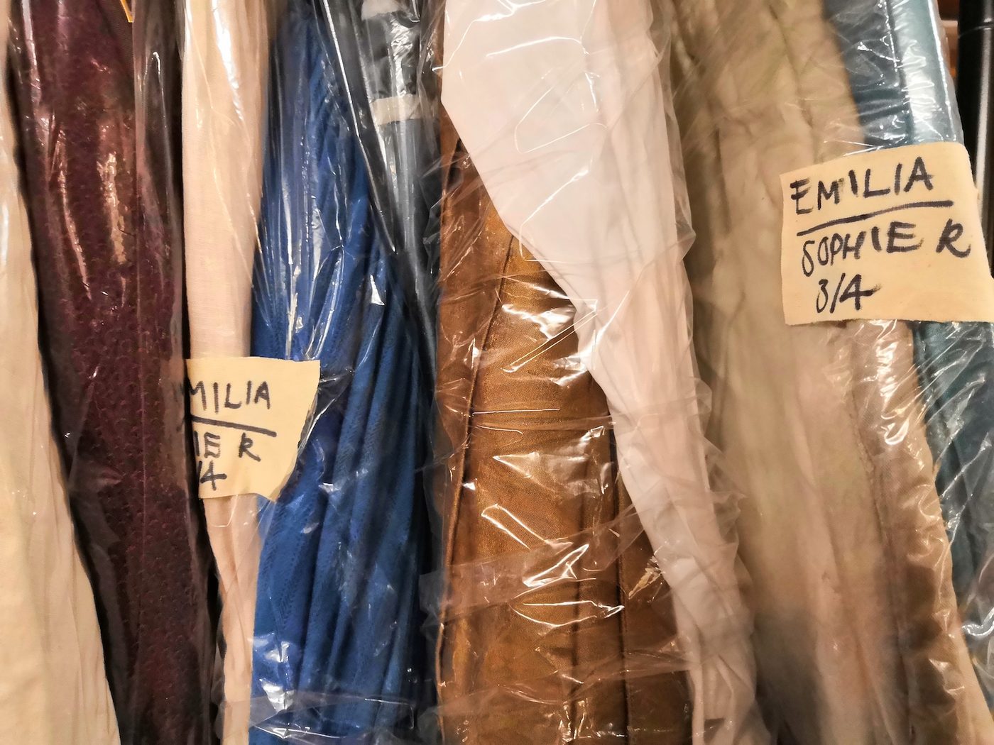 Costumes in a theatre are wrapped in film and sit next to each other on a rail