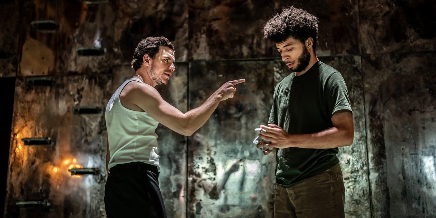 An actor points angrily at another, who stares at their hands.