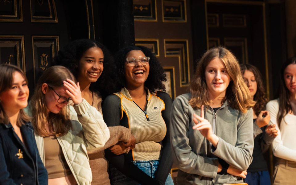 Young people laughing in a workshop. They are on stage in the Sam Wanamaker Playhouse