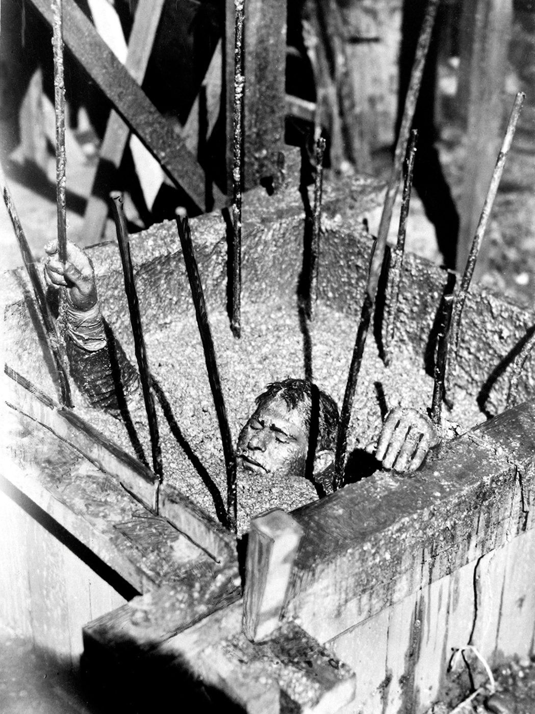 A man is buried to his neck in gravel, behind bars.