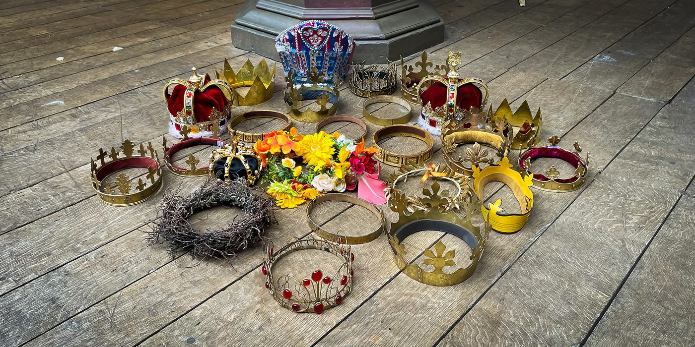 A collection of crowns sit upon the wooden stage of the Globe Theatre.