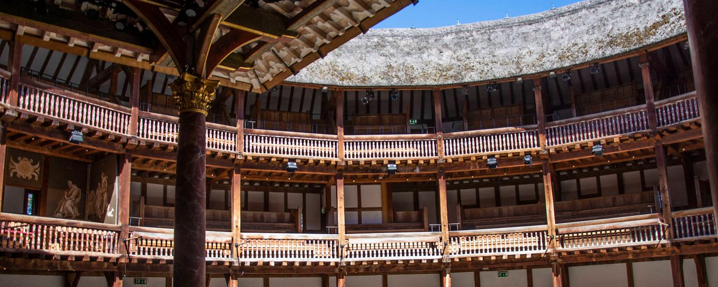 Sunlight streams into the yard of a wooden circular theatre.