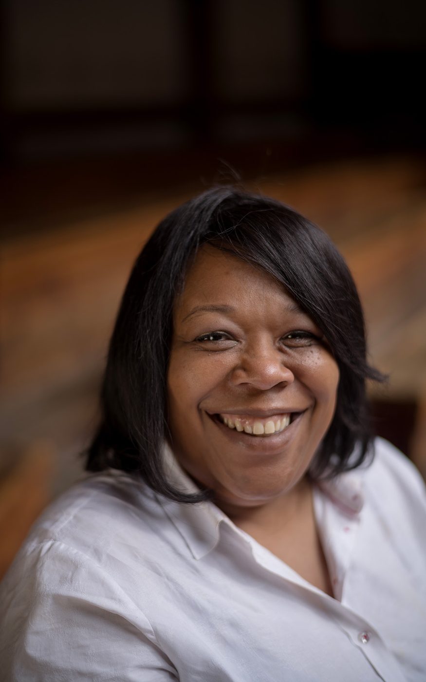 A close-up photograph of a woman sitting in the Globe Theatre, smiling to camera.