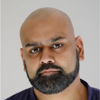 A headshot of a bald actor with a beard looking into camera