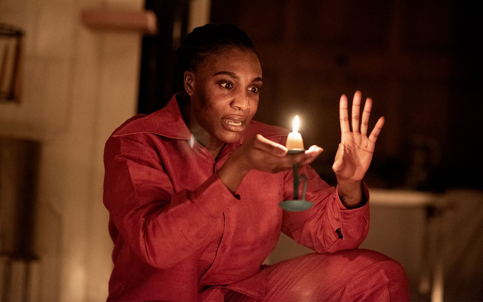 An actor looks closely at a lit candle that they hold in their hand