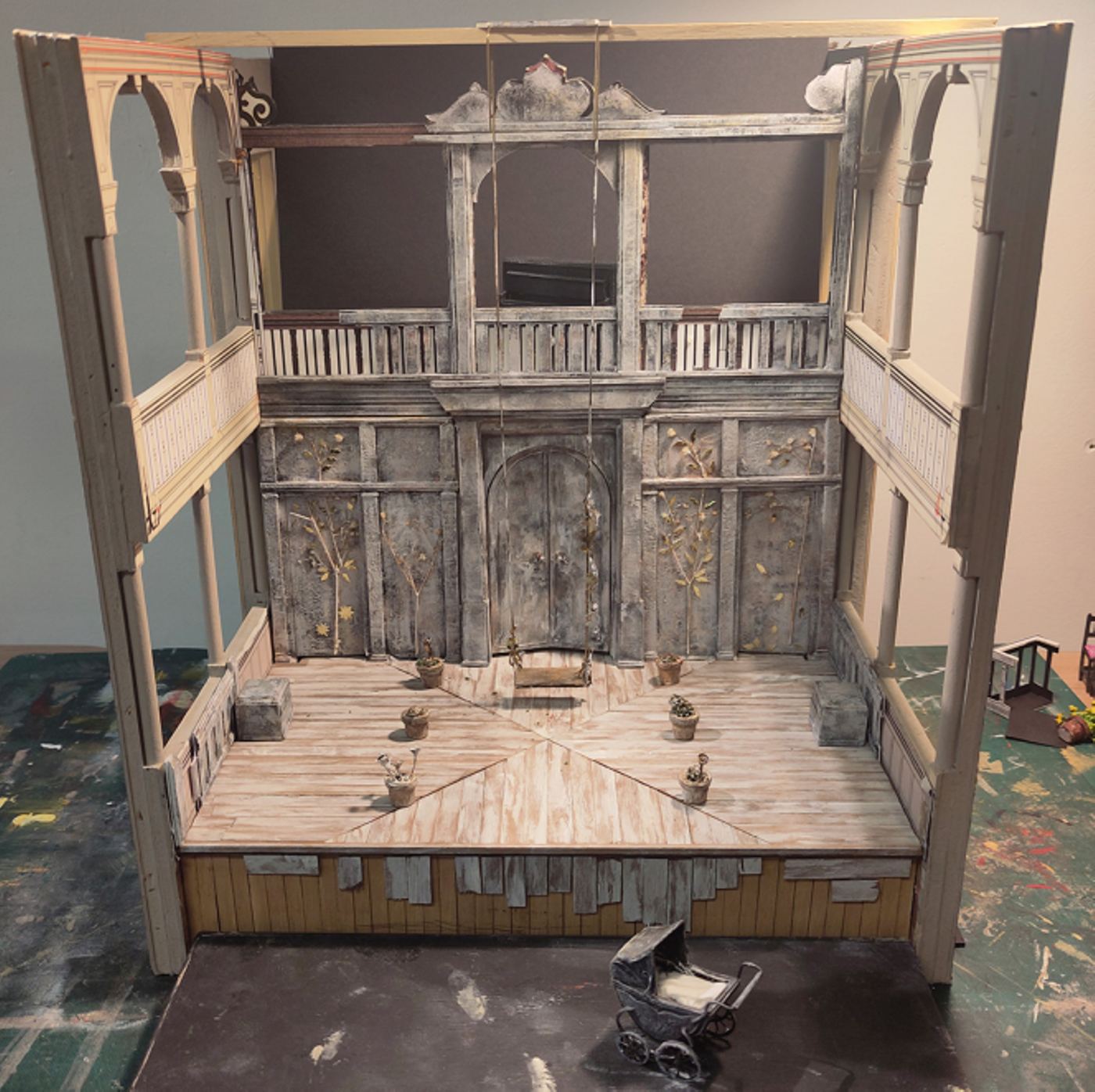 Model box set design of Three Sisters by Oli Townsend. The model shows a relatively bare set. The walls and floor of the stage have been clad in silver birch, and on the back wall there are four silver birch trees depicted, with gold leaves. A swing has been lowered onto the stage from the heavens.
