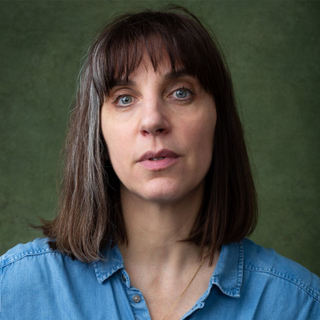 An actor with dark brown and grey hair and blue eyes looking into camera