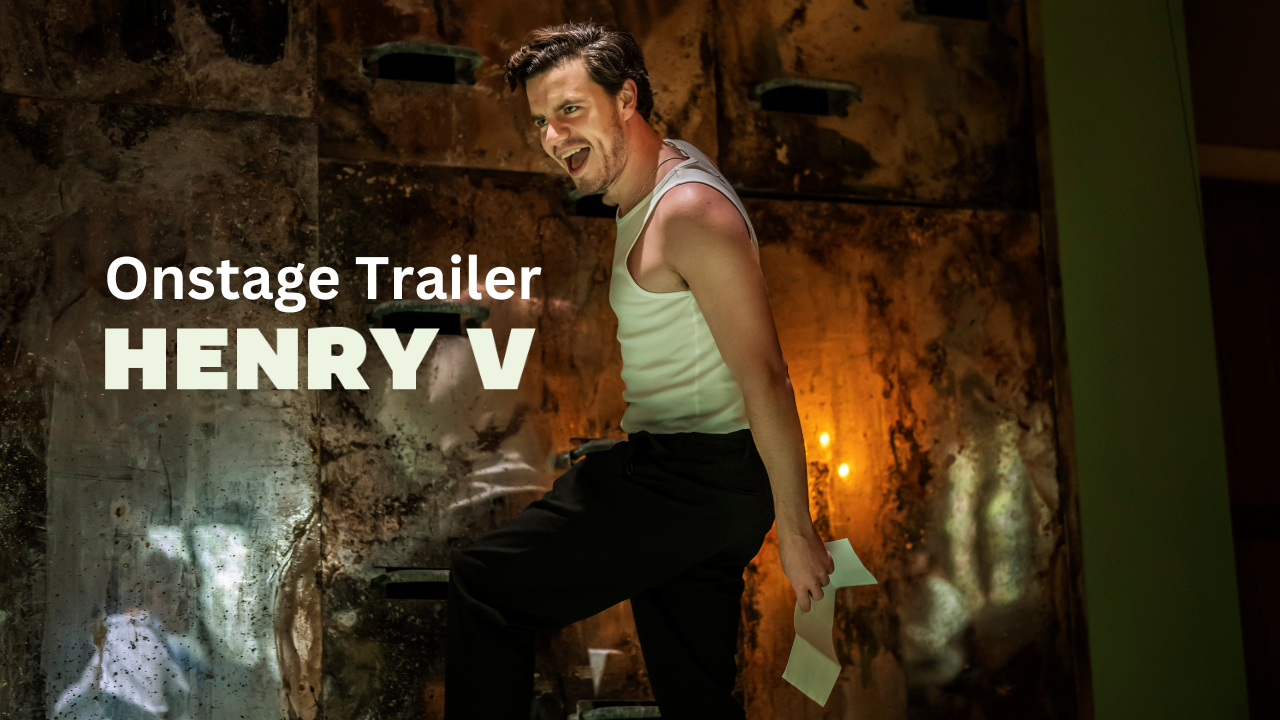 An actor in a white vest and dark trousers smiles menacingly