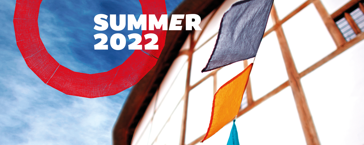 Coloured flag bunting waves in the wind outside a white building set against a blue summer sky